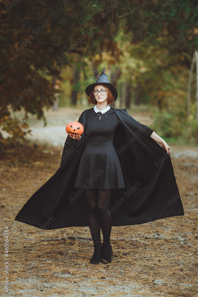 Halloween witch. Portrait of a girl in a hat and a witch costume with a pumpkin in the forest. Ready for the holiday