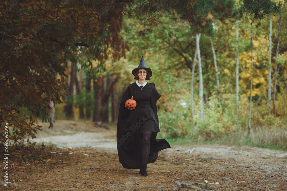 Halloween witch. Portrait of a girl in a hat and a witch costume with a pumpkin in the forest. Ready for the holiday
