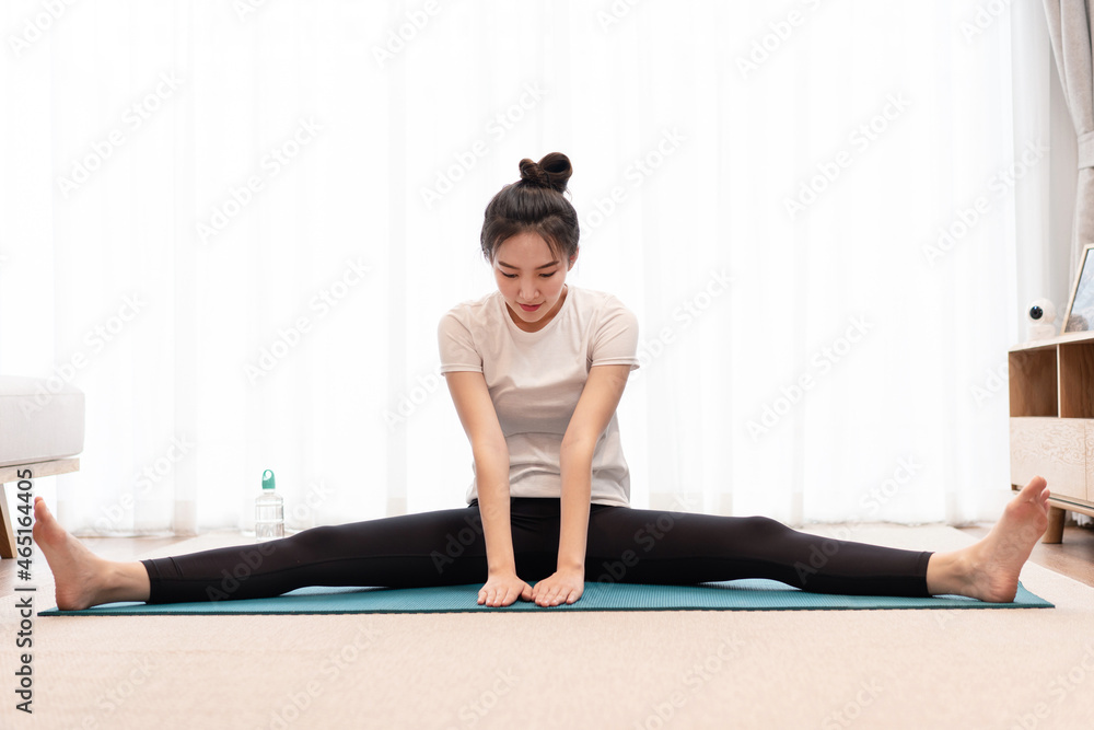 Productive activity concept a fit girl sitting on the mat open each leg to the opposite side looking concentrated on her exercise Productive activity concept a fit girl sitting on the mat open each leg to the opposite side looking concentrated on her exercise