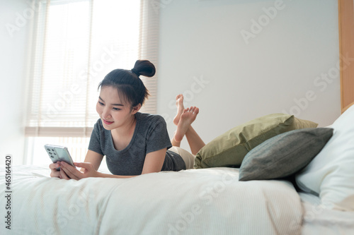 Bedroom concept a girl laying her back on several big and comfortable pillows staring on the mobile screen for the news update