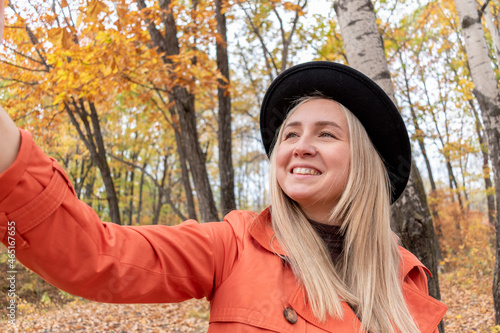 Young girl with blond hair makes a selfie on the phone while standing in the autumn forest.