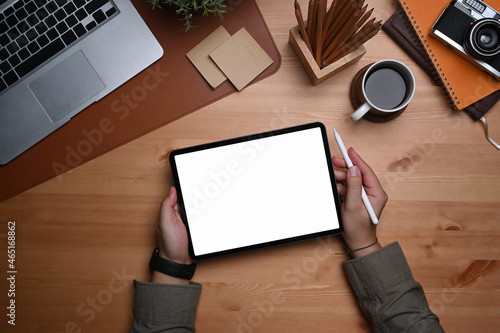 Overhead view man holding stylus pen and digital tablet with empty screen on wooden table.