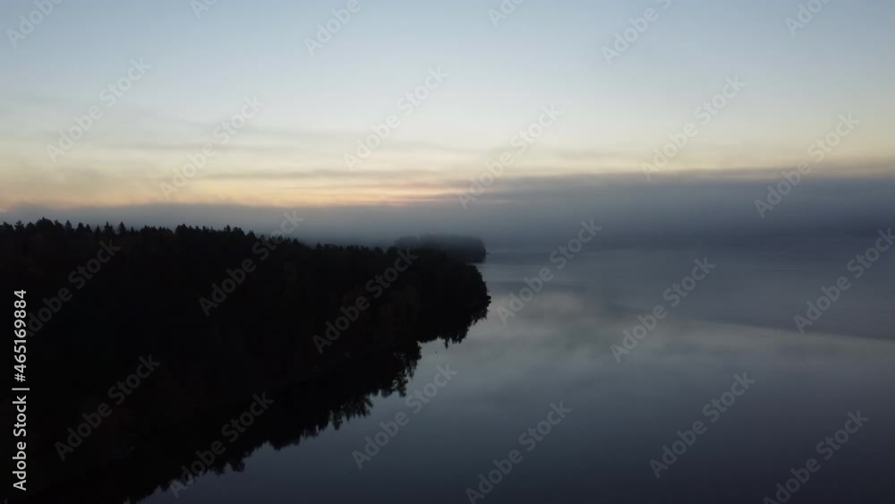 Aerial forward flight of dark forest and hovering mist over calm river during sunset in Finland Aerial forward flight of dark forest and hovering mist over calm river during sunset in Finland