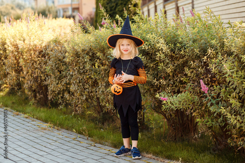 Little girl dressed in witch costume with jack o lantern celebrating Halloween outdoors, trick or treat.  photo