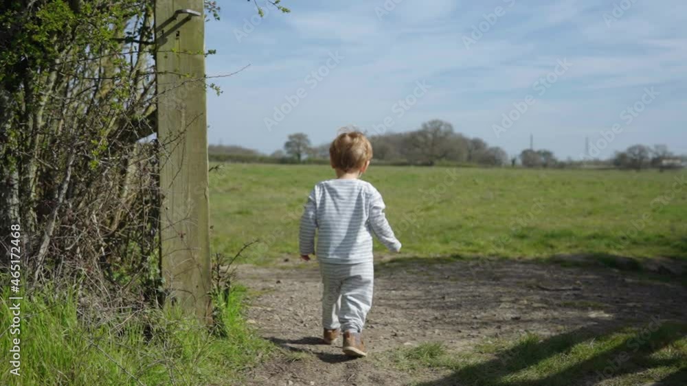 Toddler boy walks through wooden gate and runs through field, sunny day Toddler boy walks through wooden gate and runs through field, sunny day