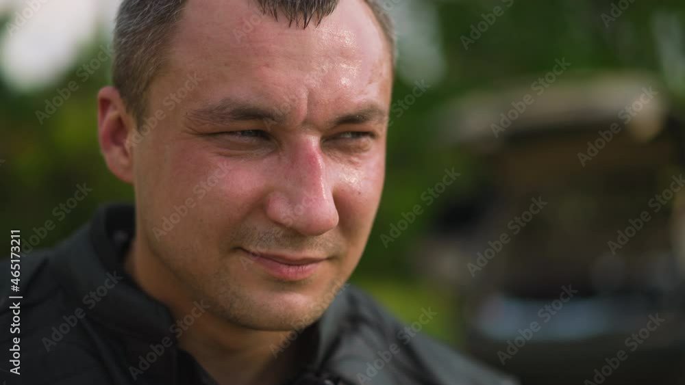 Tranquil middle aged man wearing black leather jacket looks aside standing on blurred background on sunny day close view slow motion Tranquil middle aged man wearing black leather jacket looks aside standing on blurred background on sunny day close view slow motion