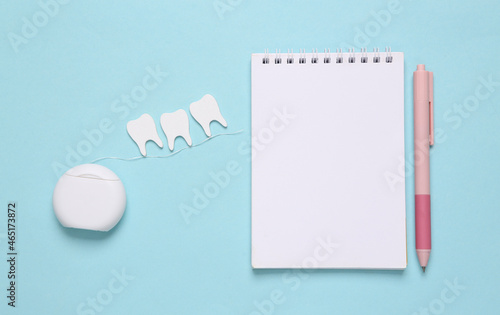 Dental care concept. Dental floss with teeth and notebook on blue background. Top view. Flat lay