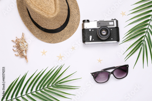 Travel flat lay. Hat with sungglasses, starfish, seashells and camera, palm leaves on white background. Top view photo