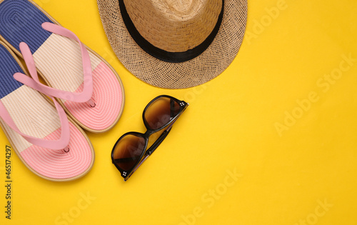 Straw hat with sunglasses and flip flops on yellow background. Top view. Copy space