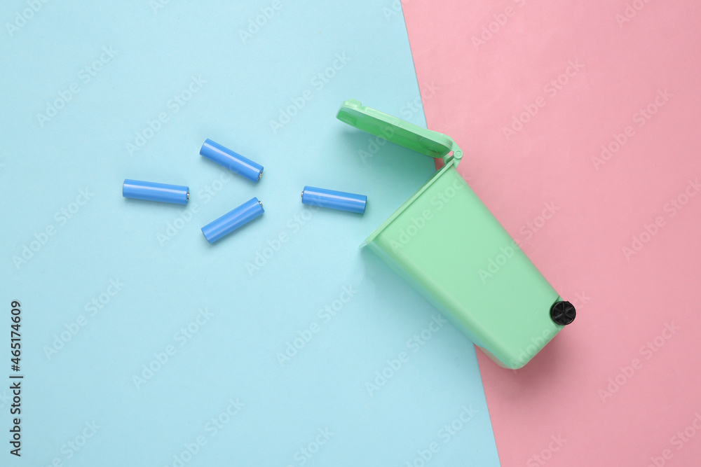 Battery recycling concept. Miniature trash can with aa batteries on blue pink background. Top view Battery recycling concept. Miniature trash can with aa batteries on blue pink background. Top view