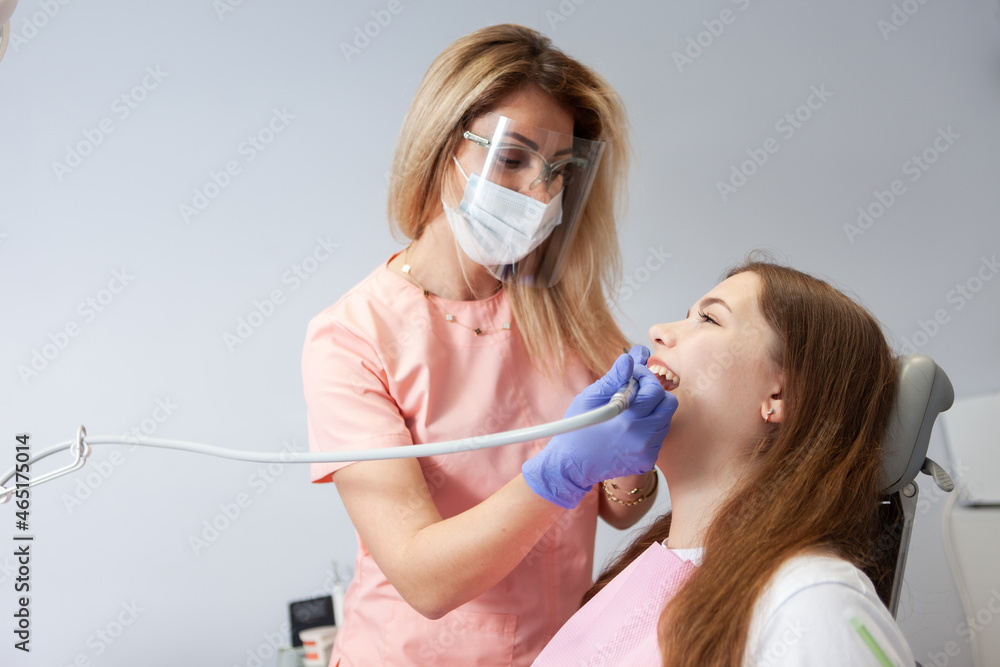 Dentists using dental drill while examining girl's mouth in clinic. Professional treatment at dental clinic Dentists using dental drill while examining girl's mouth in clinic. Professional treatment at dental clinic