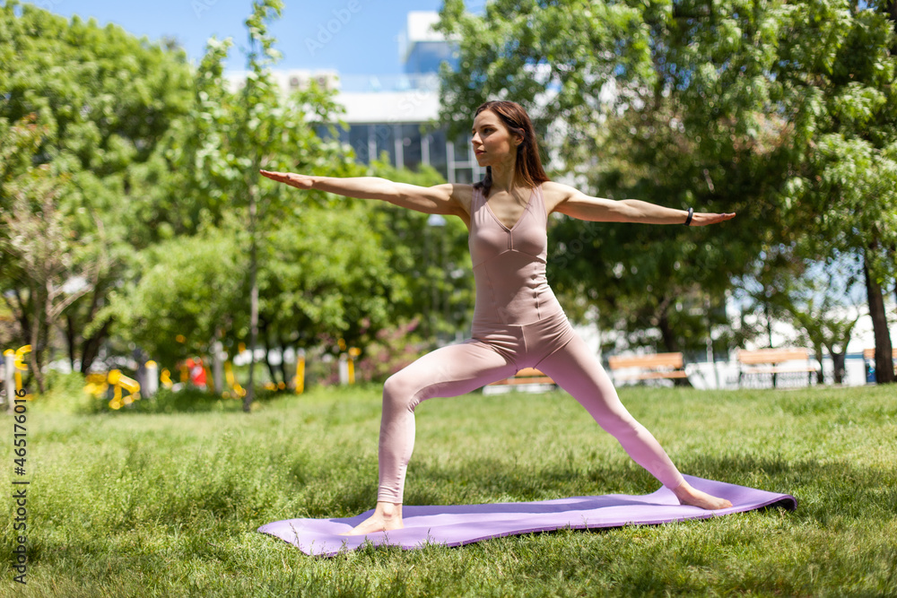 Fototapeta premium Yoga hatha. Beautiful woman practicing yoga asanas outdoors on park, keeping balance and muscle tension while doing pose. Against fresh green grass