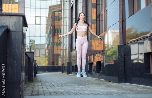 Fit woman practicing jumping rope against the background of a city building. Healthy lifestyle. Cardio workout