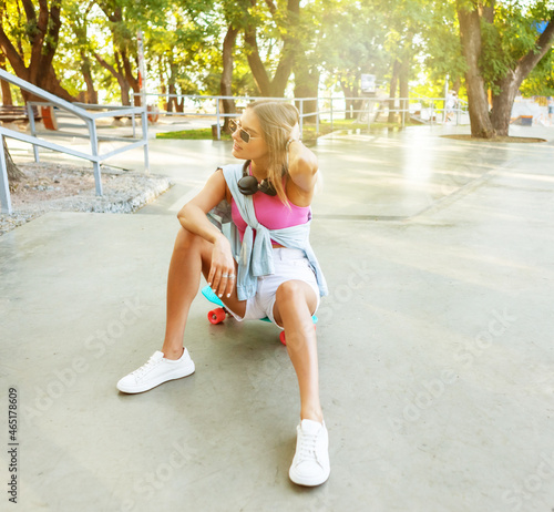 Stylish young woman dressed in summer youth clothing sits on a skateboard in a skatepark