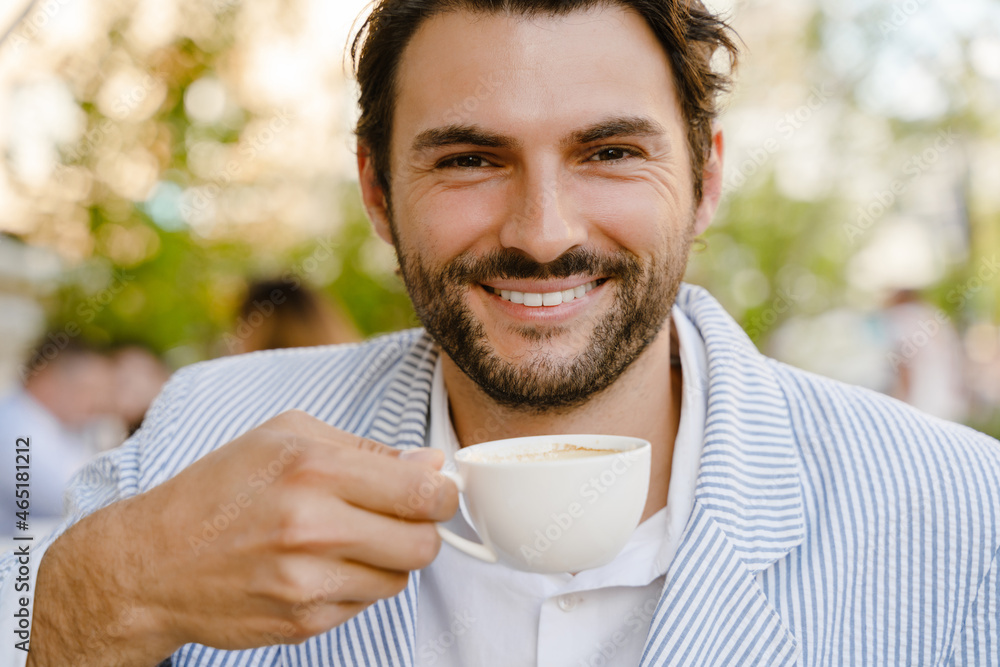 Young brunette man smiling and drinking coffee while sitting at cafe Young brunette man smiling and drinking coffee while sitting at cafe
