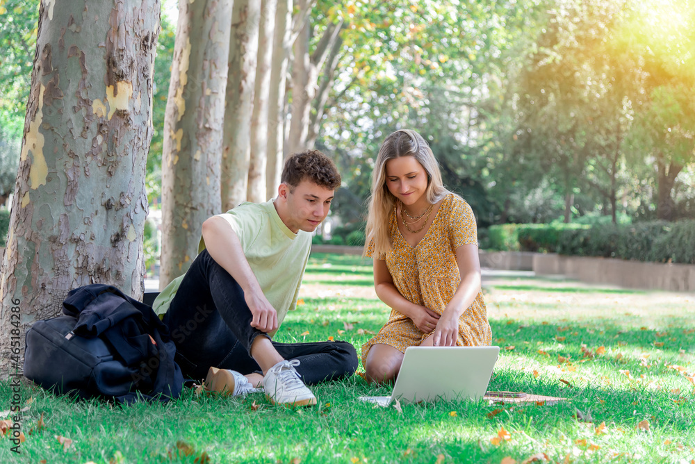 Two young college students sitting on the campus lawn studying with a laptop computer Two young college students sitting on the campus lawn studying with a laptop computer
