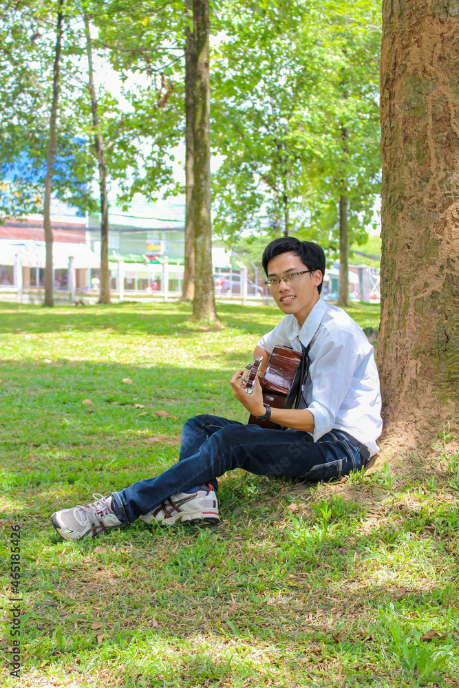 A young Vietnamese man playing the guitar near a big tree A young Vietnamese man playing the guitar near a big tree