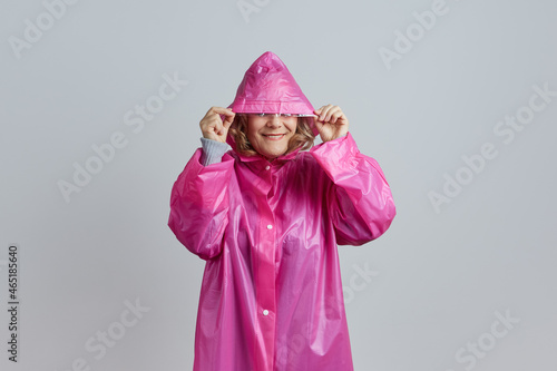 Senior happy woman in magenta raincoat hides her face from the rain under the hood