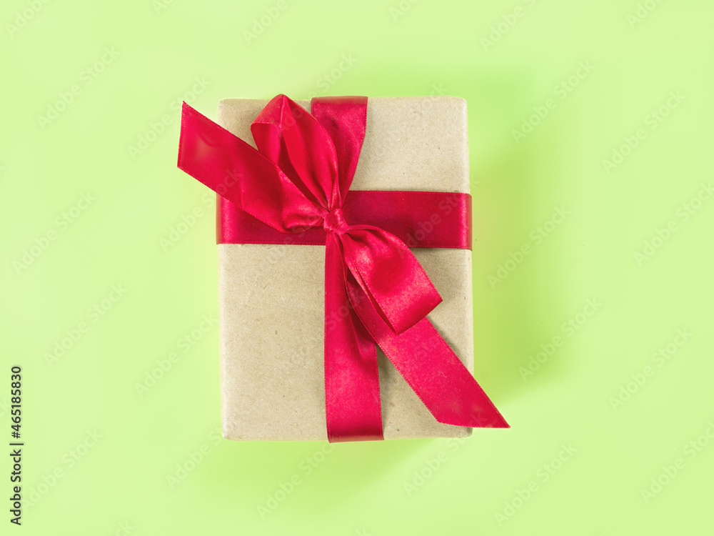 The above view on the packed present in the craft paper with the red satin ribbon on the light green background. The above view on the packed present in the craft paper with the red satin ribbon on the light green background.