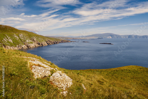View on amazing Keem bay from a top of a mountain. Warm sunny day. White clouds on blue sky. Spectacular Irish nature landscape. Achill island, Ireland. Nobody. Cliffs and coast line.