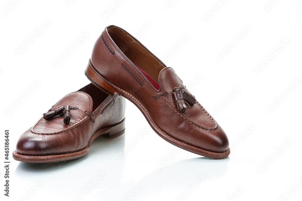 Footwear Concepts. Pair of Traditional Formal Stylish Brown Pebble Grain Tassel Loafer Shoes On White Reflective Surface. Footwear Concepts. Pair of Traditional Formal Stylish Brown Pebble Grain Tassel Loafer Shoes On White Reflective Surface.