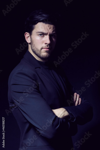 Portrait of Handsome Caucasian Brunet Businessman Wearing Black Suit Posing With Hands folded Against Black
