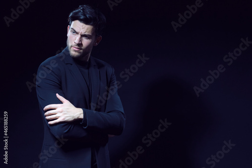 Portrait of Serious Handsome Caucasian Brunet Businessman Wearing Black Suit Posing With Folded Hands Looking Aside Against Black Studio Background.