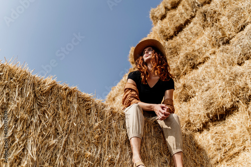 Woman wearing hat sitting on haystack in farm photo