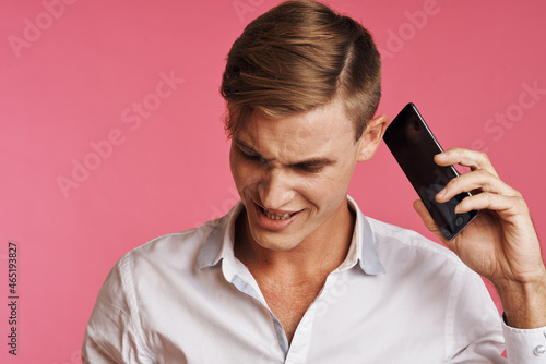 portrait of a man in a white shirt talking on the phone pink background