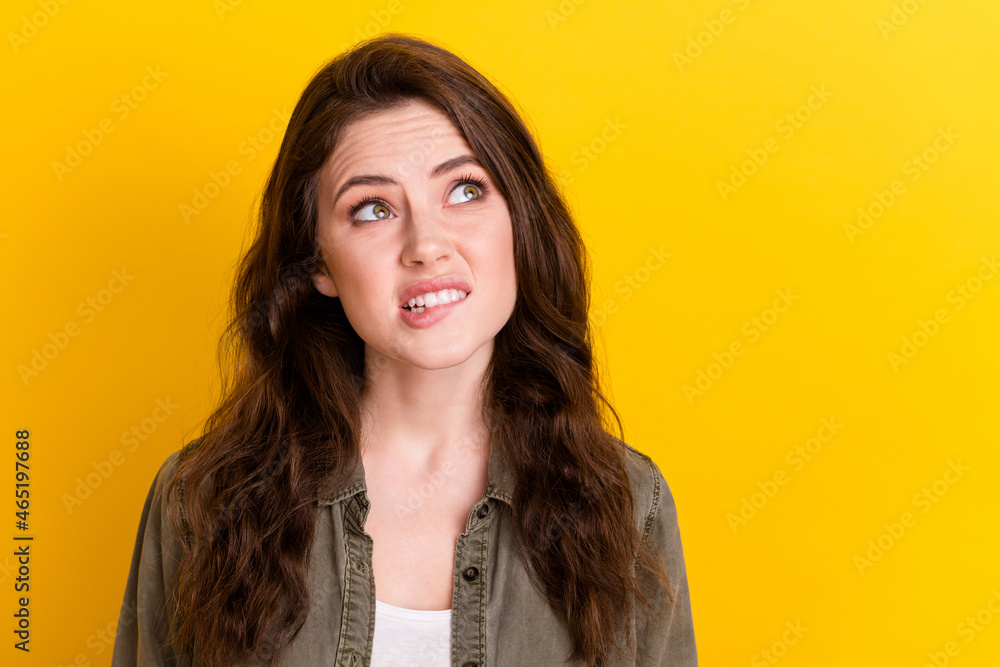 Fototapeta premium Photo of funny guilty young lady wear brown shirt biting lip looking empty space isolated yellow color background
