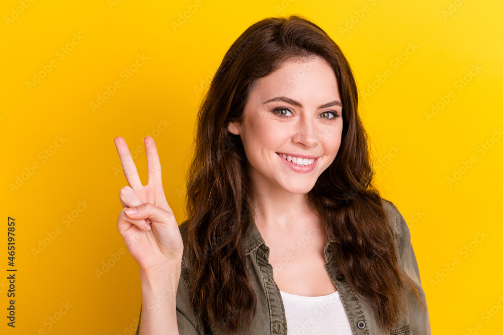Photo of satisfied young girl beaming smile fingers show v-sign symbol look camera isolated on yellow color background Photo of satisfied young girl beaming smile fingers show v-sign symbol look camera isolated on yellow color background