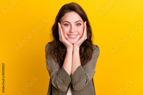 Portrait of attractive cheerful pleased girl touching face enjoying isolated over bright yellow color background