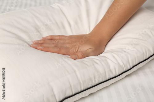 Woman touching soft pillow on bed, closeup