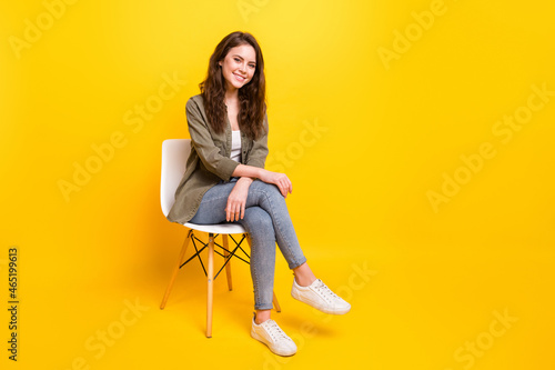 Portrait of attractive cheerful girl sitting on office hair resting waiting isolated over bright yellow color background