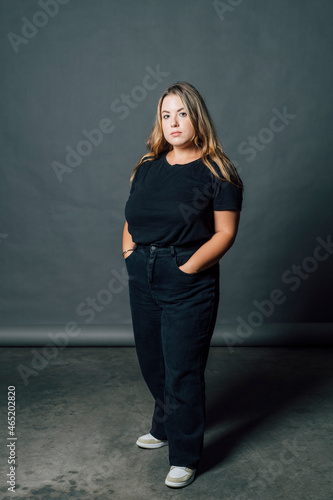 Plus size woman standing with hands in pockets by gray backdrop photo