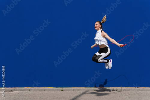 Female athlete jumping rope in front of blue wall