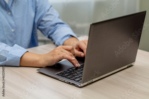 A woman in a blue shirt is typing on a laptop. The right female hand is in focus. Horizontal view.
