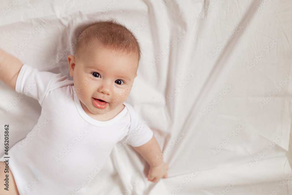 charming newborn baby in a white bodysuit lies on his back on a white fabric. top view. products for children. concept of happy childhood and motherhood. space for text. High quality photo charming newborn baby in a white bodysuit lies on his back on a white fabric. top view. products for children. concept of happy childhood and motherhood. space for text. High quality photo