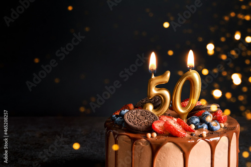 Chocolate birthday cake with berries, cookies and number fifty golden candles on black background, copy space photo