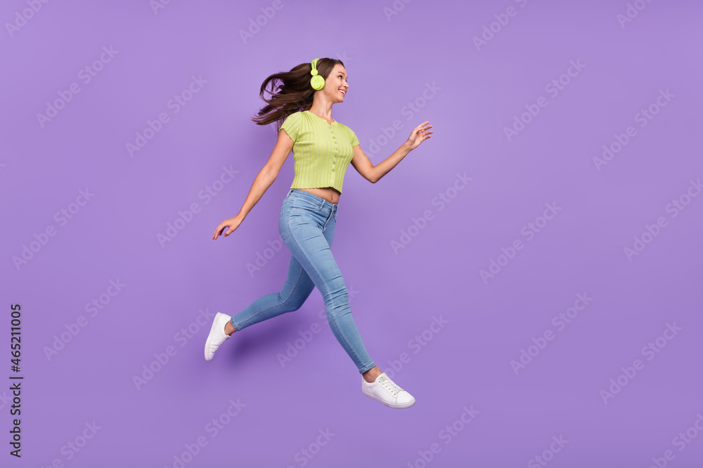 Full length body size view of lovely cheerful girl jumping listening pop single going isolated over purple violet color background Full length body size view of lovely cheerful girl jumping listening pop single going isolated over purple violet color background