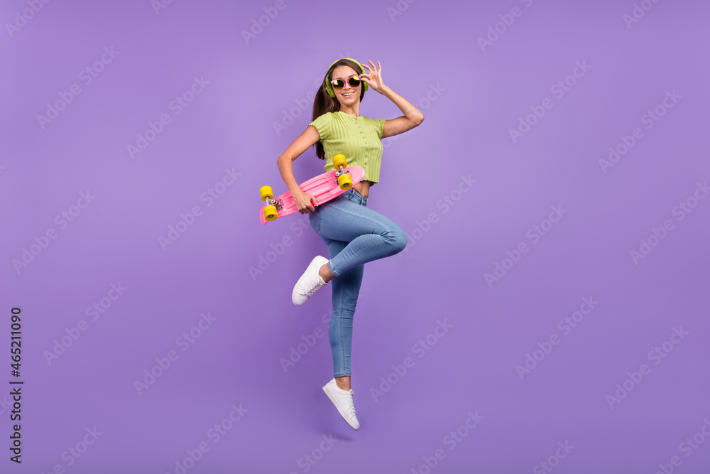 Full length body size view of nice cheerful girl jumping listening pop dancing with skate isolated over purple violet color background Full length body size view of nice cheerful girl jumping listening pop dancing with skate isolated over purple violet color background