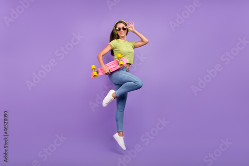 Full length body size view of nice cheerful girl jumping listening pop dancing with skate isolated over purple violet color background