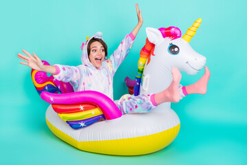 Photo of adorable funky young woman dressed unicorn nightwear smiling riding bloated circle isolated teal color background