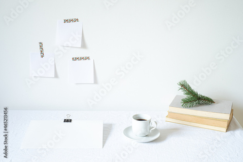 Christmas or New Year breakfast scene. Notepad mockup of good intentions. Blank note paper hanging on the wall.Books, coffee cup, empty paper sheet on the desk.Working space, home office concept
