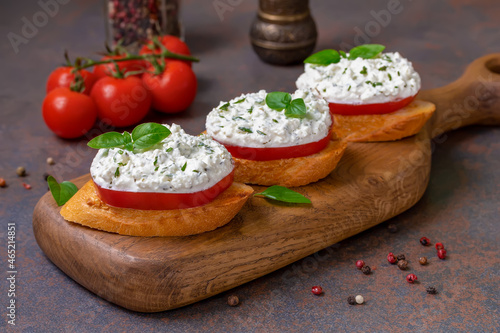 Fresh Tomato Bruschetta topped with Herbed Ricotta and basil leaves served on wooden board.  Dark background, selective focus. 