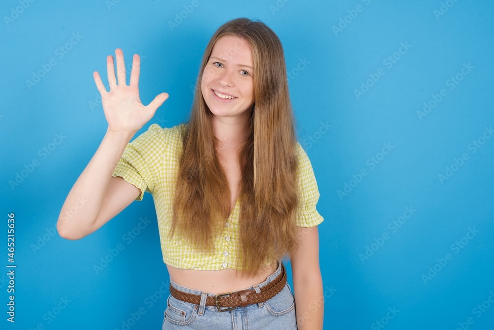 young ukranian girl wearing yellow t-shirt over blue backaground showing and pointing up with fingers number five while smiling confident and happy. young ukranian girl wearing yellow t-shirt over blue backaground showing and pointing up with fingers number five while smiling confident and happy.