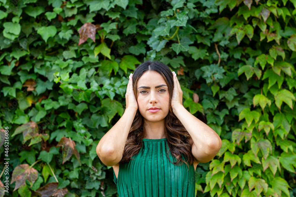 Beautiful woman covering ears with hands in front of green ivy plants Beautiful woman covering ears with hands in front of green ivy plants