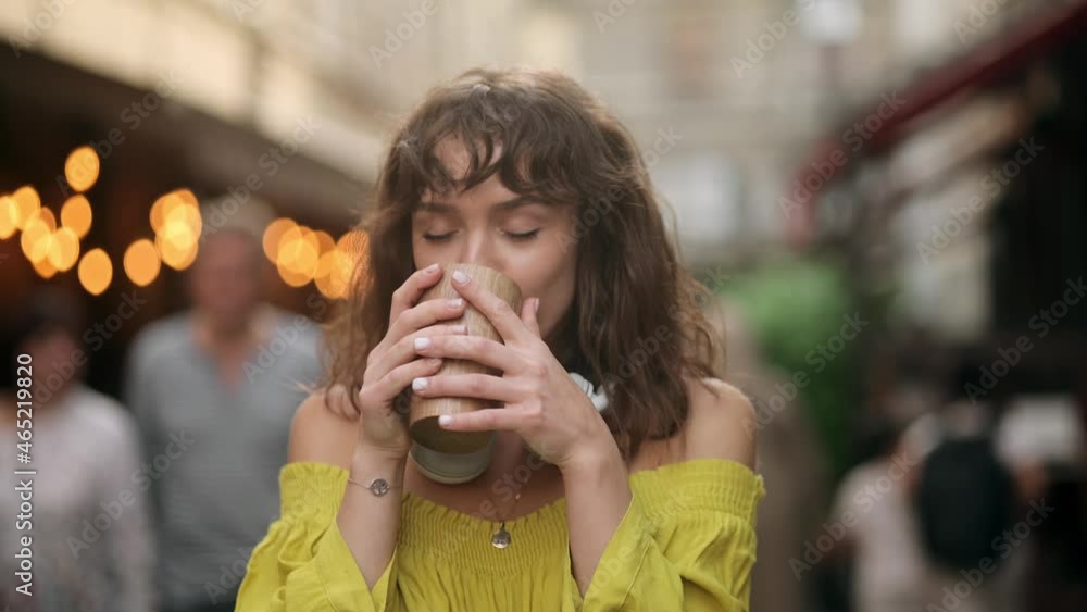 Young pretty woman with curly hair drinking coffee. Natural beauty pretty woman with curly hair, girl taking a sip of coffee or tea from eco cup, on warm summer evening sunset in big city Young pretty woman with curly hair drinking coffee. Natural beauty pretty woman with curly hair, girl taking a sip of coffee or tea from eco cup, on warm summer evening sunset in big city