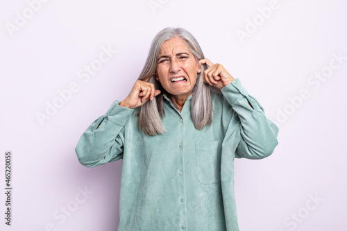 middle age gray hair woman looking angry, stressed and annoyed, covering both ears to a deafening noise, sound or loud music photo