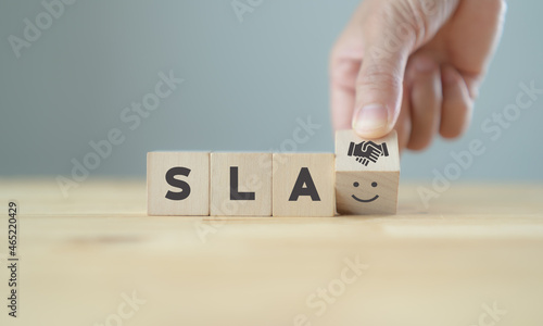 SLA - Service Level Agreement acronym, business concept. Service performance tracking to reduce the uncertainty the customer in process. Hand flips  wood cube with SLA to customer satisfaction symbols photo